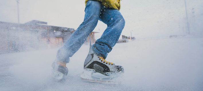 Close up photo of skates cutting into ice to stop, spraying snow towards camera. On an outdoor rink.